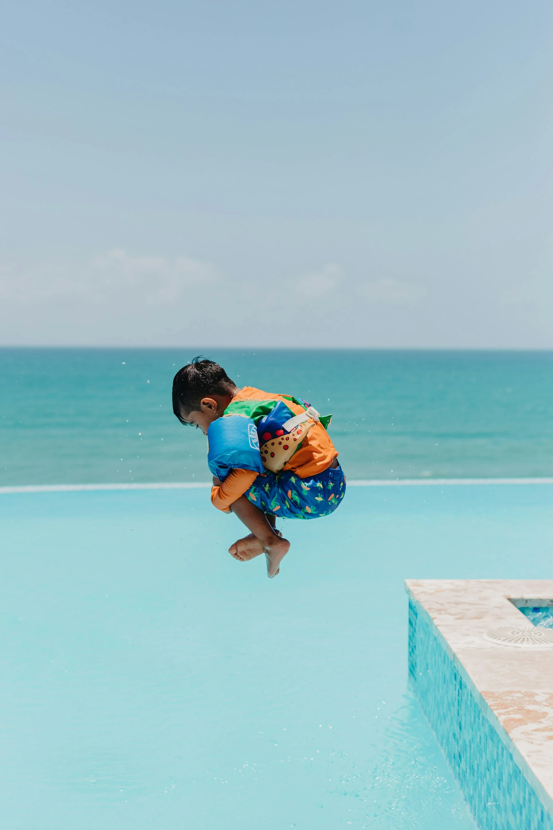 Child mid-jump over an infinity pool with the ocean horizon behind